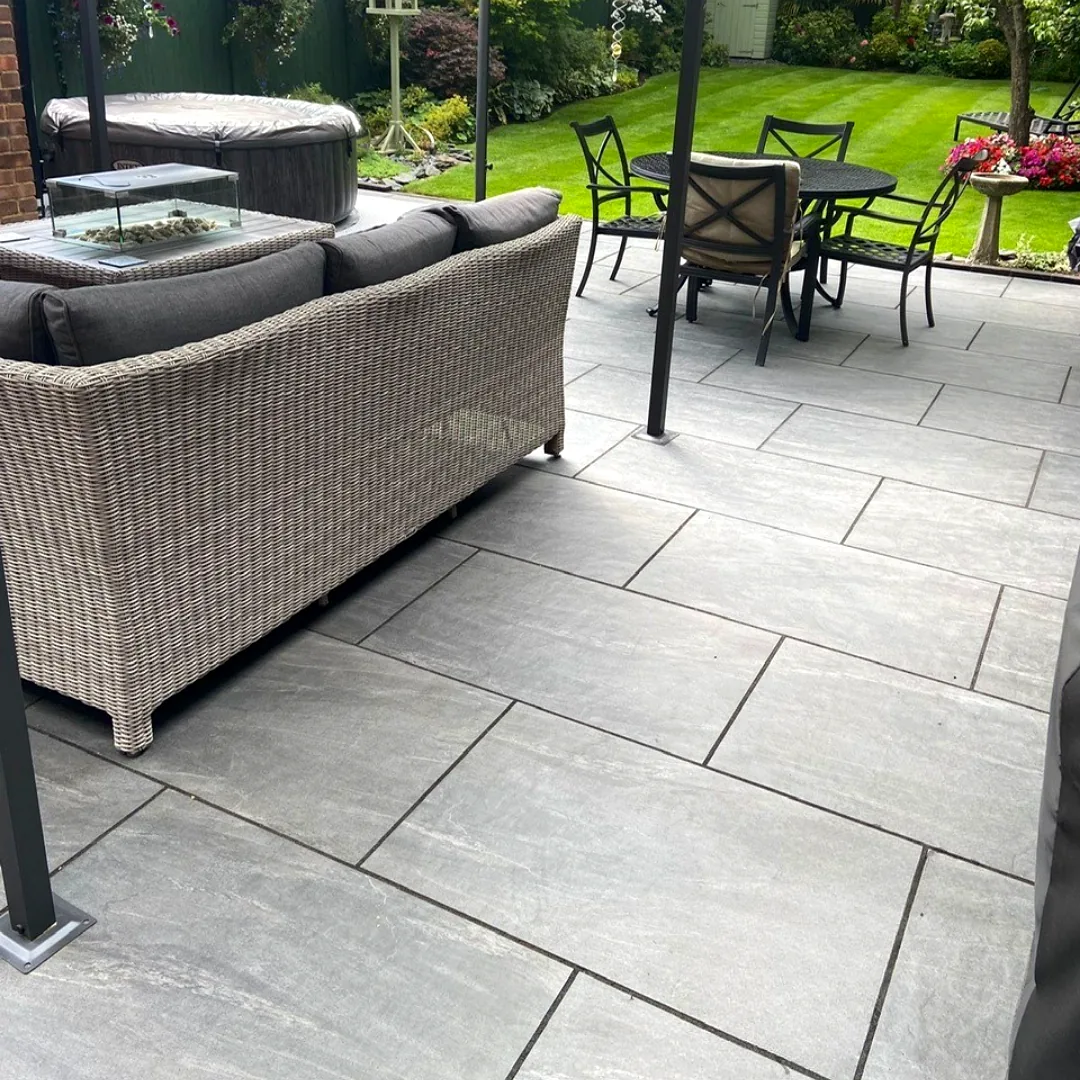 Grey porcelain patio with sofa and dining set overlooking lawn
