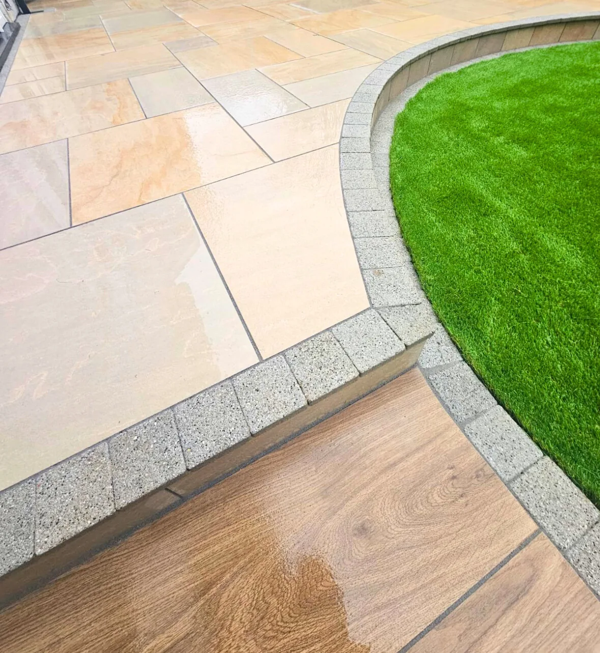 Clean Indian sandstone patio with block edging beside artificial lawn